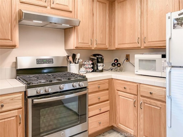 kitchen with exhaust hood, tile counters, light brown cabinets, and white appliances