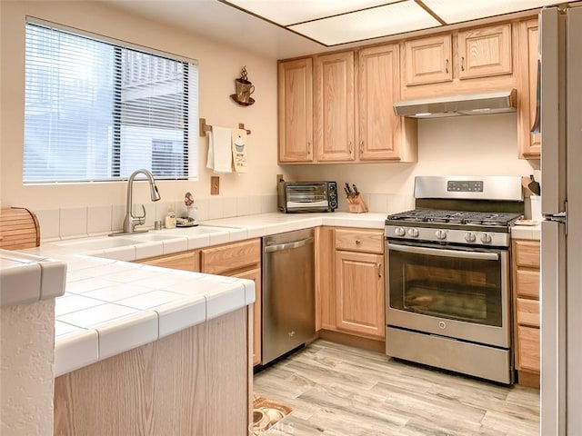 kitchen with light hardwood / wood-style floors, extractor fan, stainless steel appliances, tile counters, and light brown cabinets