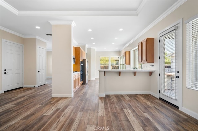 kitchen with dark hardwood / wood-style flooring, stainless steel appliances, a kitchen breakfast bar, ornamental molding, and kitchen peninsula