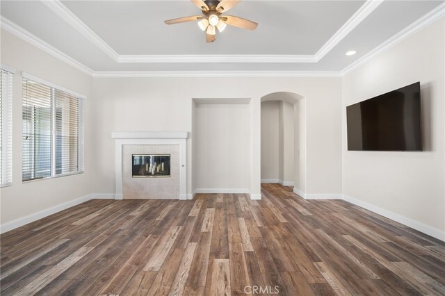 unfurnished living room featuring dark wood-type flooring, crown molding, a tiled fireplace, and ceiling fan