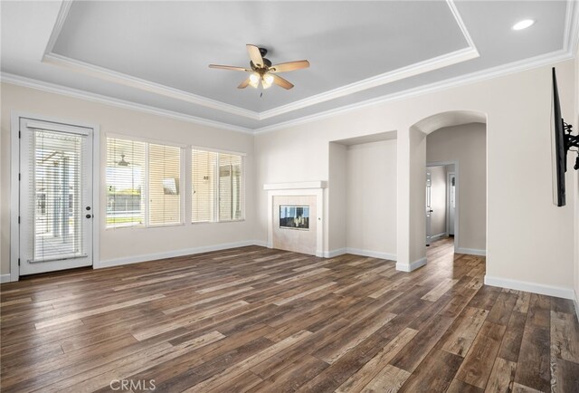 unfurnished living room featuring ceiling fan, dark wood-type flooring, a tray ceiling, and ornamental molding