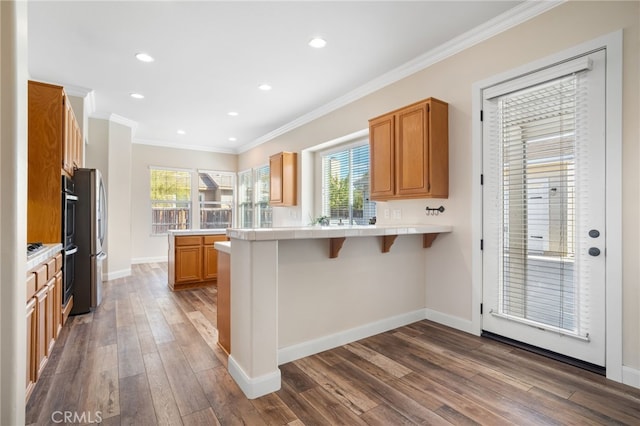 kitchen with dark wood-type flooring, a healthy amount of sunlight, a kitchen breakfast bar, ornamental molding, and kitchen peninsula