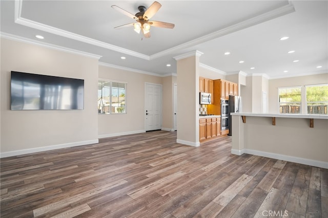 unfurnished living room featuring ceiling fan, wood-type flooring, a tray ceiling, and ornamental molding