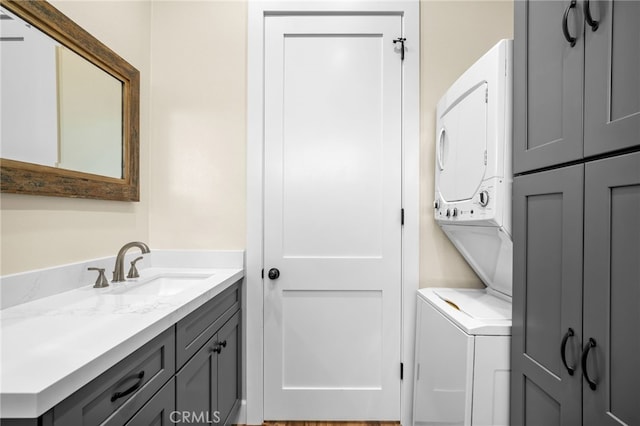 washroom with stacked washing maching and dryer, cabinets, and sink