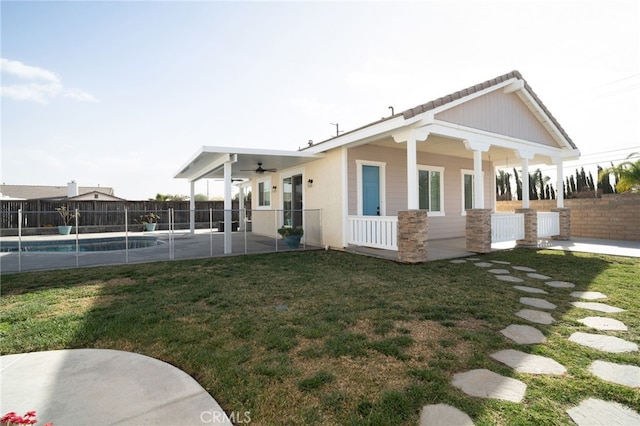 rear view of property with ceiling fan, a patio area, a fenced in pool, and a lawn