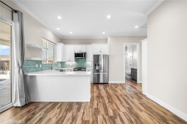 kitchen featuring white cabinetry, stainless steel appliances, sink, kitchen peninsula, and ornamental molding