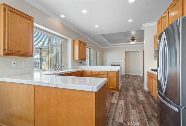 kitchen with kitchen peninsula, stainless steel refrigerator with ice dispenser, ornamental molding, tile counters, and dark hardwood / wood-style flooring