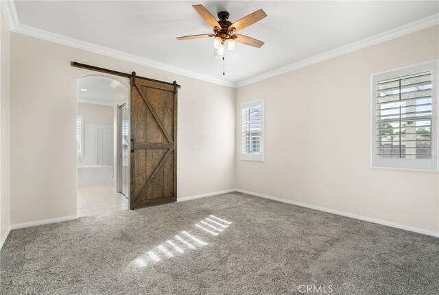 carpeted spare room featuring ceiling fan, crown molding, and a barn door