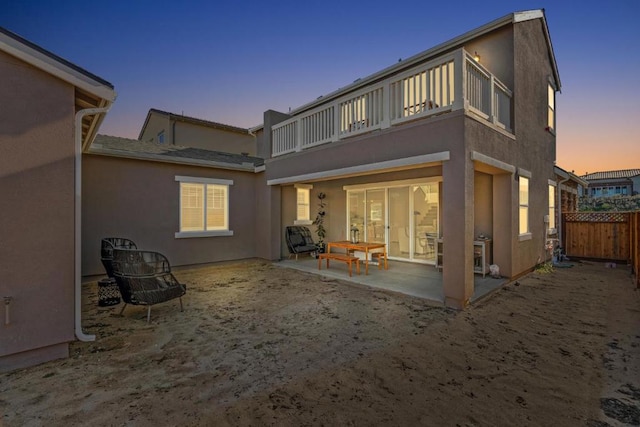 back house at dusk featuring a balcony and a patio area