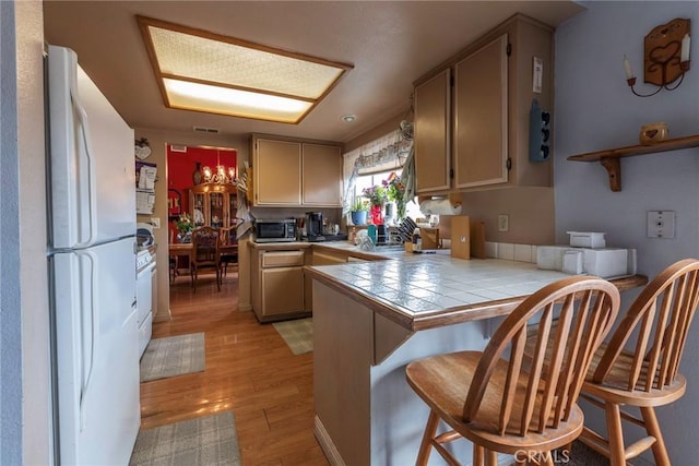 kitchen with tile countertops, a breakfast bar, kitchen peninsula, light hardwood / wood-style flooring, and white refrigerator