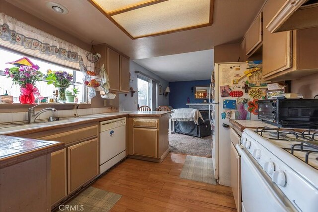 kitchen with tile countertops, kitchen peninsula, sink, white appliances, and light hardwood / wood-style flooring