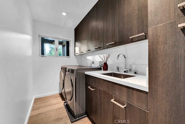 laundry room featuring light wood-type flooring, cabinets, washer and clothes dryer, and sink