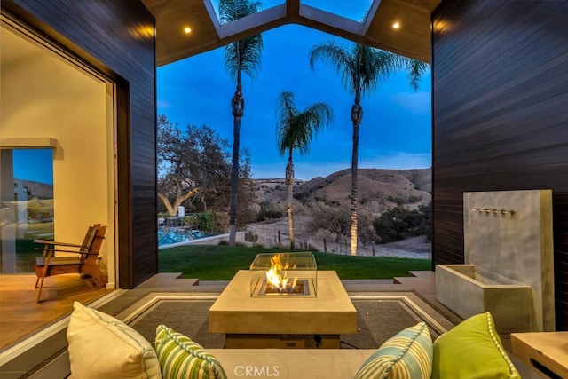 patio terrace at dusk featuring a mountain view, a fire pit, and a lawn