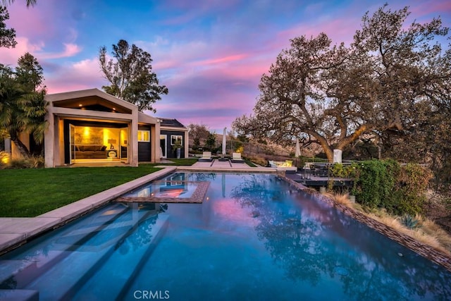 pool at dusk featuring an in ground hot tub, a lawn, and a patio