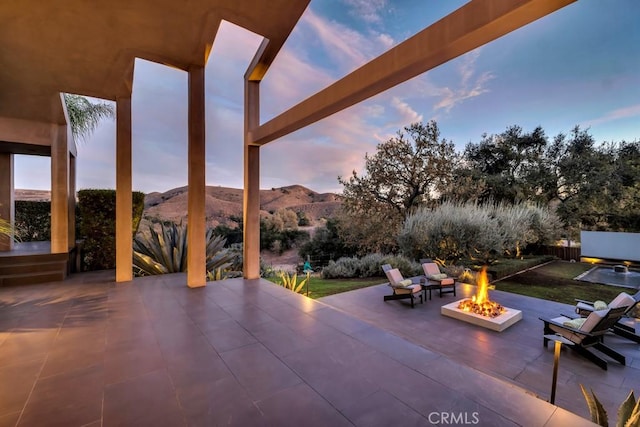 patio terrace at dusk featuring a mountain view and a fire pit