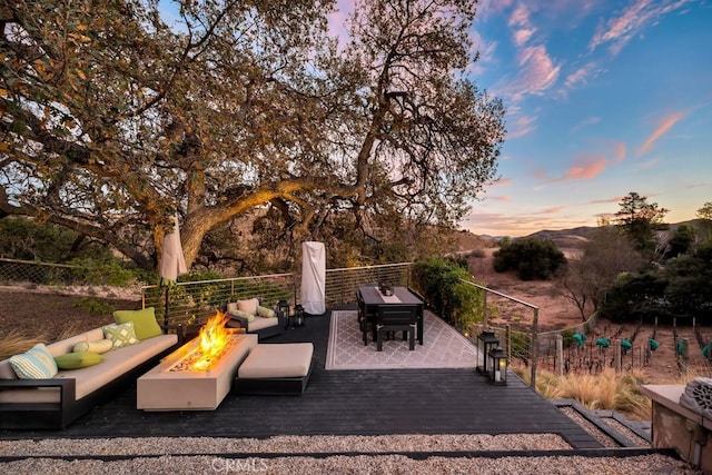 patio terrace at dusk featuring a wooden deck and an outdoor living space with a fire pit