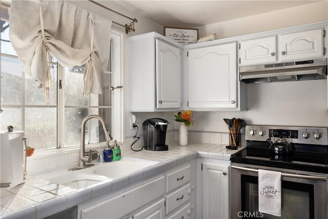 kitchen with stainless steel electric range, tile counters, and white cabinetry