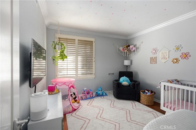 bedroom with a nursery area, hardwood / wood-style flooring, and crown molding