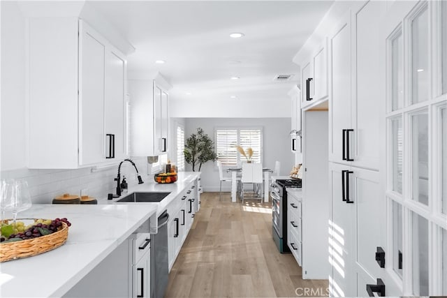 kitchen featuring light stone countertops, white cabinets, stainless steel appliances, tasteful backsplash, and light hardwood / wood-style floors