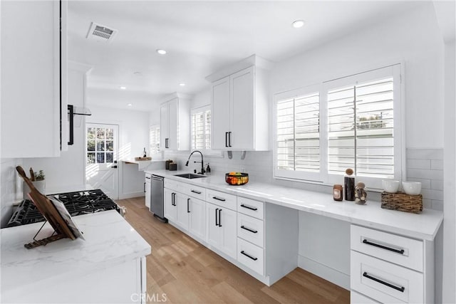 kitchen with light hardwood / wood-style floors, light stone countertops, stainless steel dishwasher, white cabinets, and sink