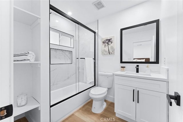 full bathroom featuring hardwood / wood-style floors, shower / bath combination with glass door, vanity, and toilet