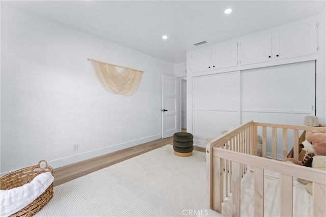 bedroom featuring light hardwood / wood-style flooring, a closet, and a crib