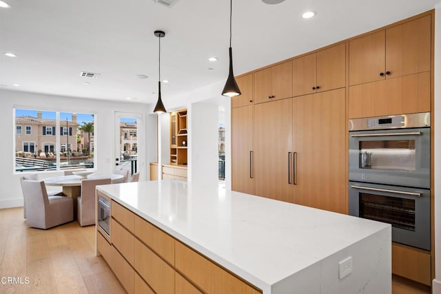 kitchen featuring decorative light fixtures, stainless steel double oven, light wood-type flooring, and a large island