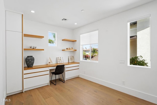 home office with light hardwood / wood-style flooring and built in desk