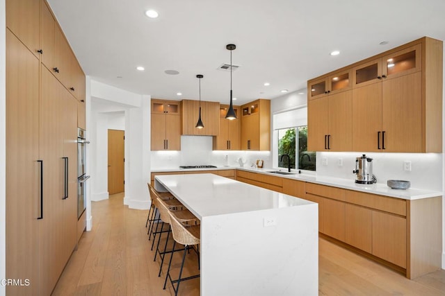 kitchen featuring a center island, stovetop, sink, hanging light fixtures, and light wood-type flooring