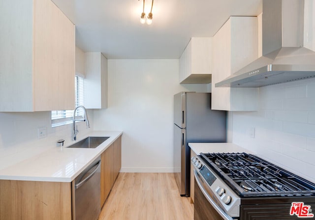 kitchen with wall chimney range hood, stainless steel appliances, sink, backsplash, and light hardwood / wood-style flooring