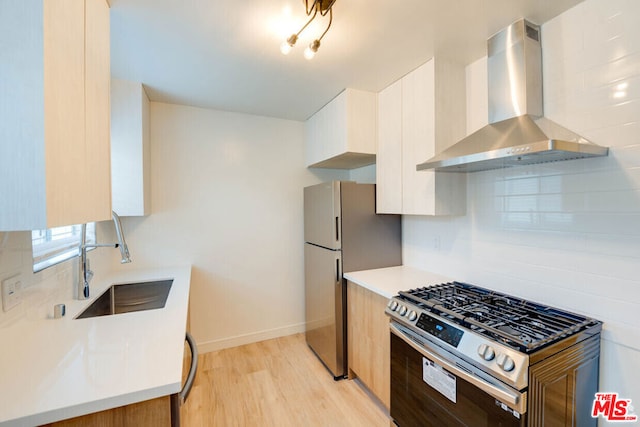 kitchen with light hardwood / wood-style floors, sink, appliances with stainless steel finishes, white cabinets, and wall chimney exhaust hood