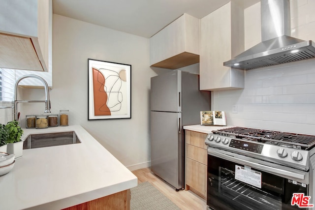 kitchen with light hardwood / wood-style floors, stainless steel appliances, tasteful backsplash, wall chimney range hood, and sink