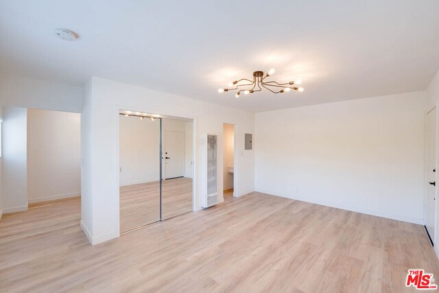 unfurnished bedroom with electric panel, a notable chandelier, and light wood-type flooring