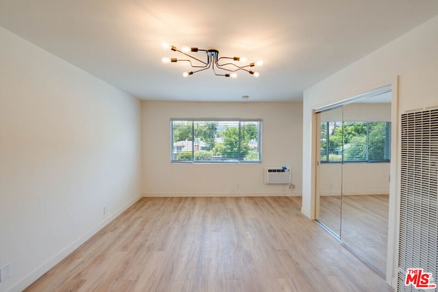 unfurnished bedroom with a wall mounted AC, a closet, a notable chandelier, and light hardwood / wood-style flooring