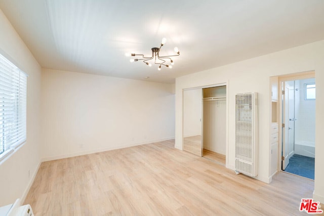 unfurnished bedroom featuring ensuite bath, an inviting chandelier, and light wood-type flooring