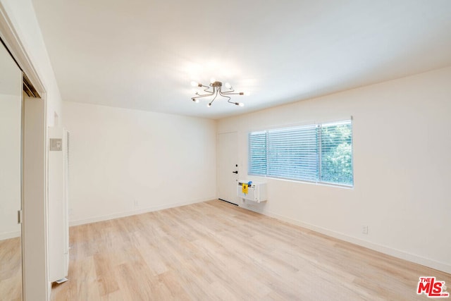 spare room featuring light wood-type flooring and a notable chandelier