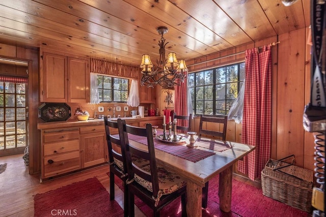 dining area with hardwood / wood-style flooring, wood walls, plenty of natural light, and a notable chandelier