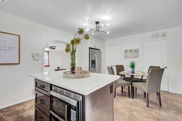 kitchen featuring appliances with stainless steel finishes, a center island, white cabinets, light tile patterned flooring, and ceiling fan with notable chandelier