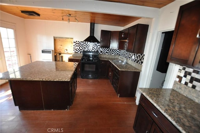 kitchen with black gas range, decorative backsplash, a center island, wall chimney exhaust hood, and sink