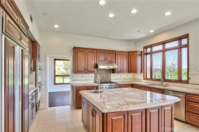 kitchen featuring decorative backsplash, a kitchen island with sink, light tile patterned flooring, dishwasher, and sink