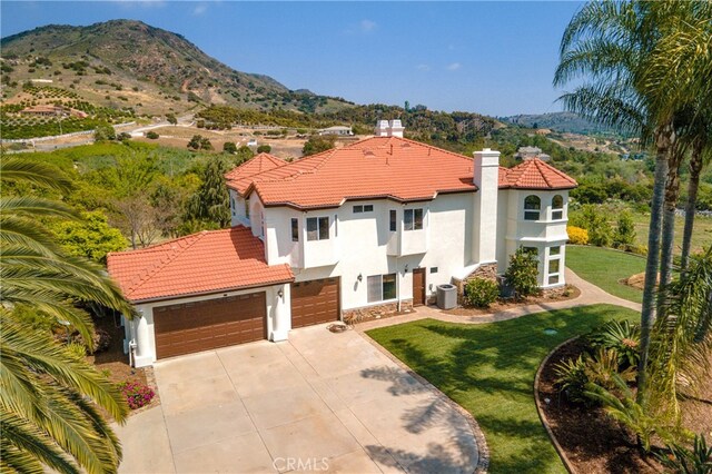 view of front facade with central air condition unit, a garage, a mountain view, and a front yard