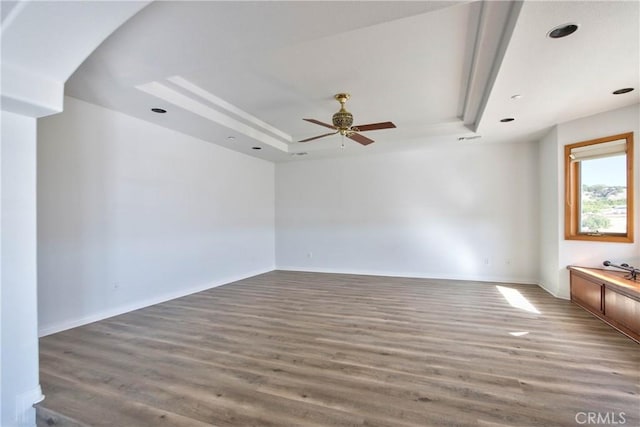 unfurnished room with a raised ceiling, ceiling fan, and dark hardwood / wood-style floors