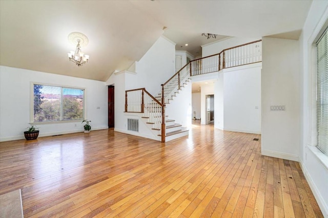 unfurnished living room with light hardwood / wood-style floors, high vaulted ceiling, and a chandelier