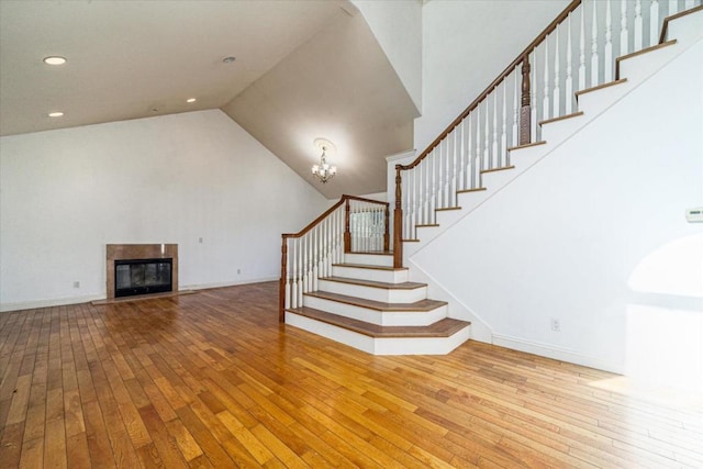 stairway with high vaulted ceiling, wood-type flooring, and a notable chandelier