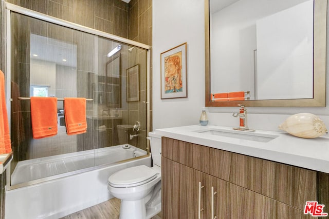 full bathroom with combined bath / shower with glass door, vanity, wood-type flooring, and toilet