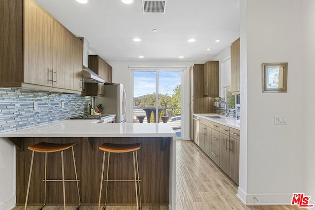 kitchen featuring kitchen peninsula, stainless steel fridge, a breakfast bar area, light hardwood / wood-style flooring, and sink