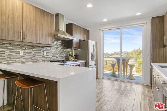 kitchen with kitchen peninsula, range, a kitchen breakfast bar, light wood-type flooring, and wall chimney exhaust hood