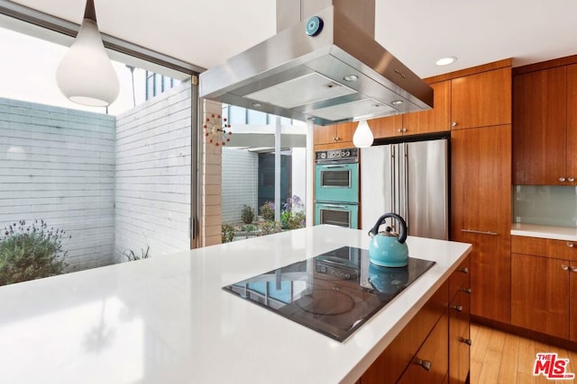 kitchen featuring decorative light fixtures, multiple ovens, high end refrigerator, island exhaust hood, and black electric cooktop