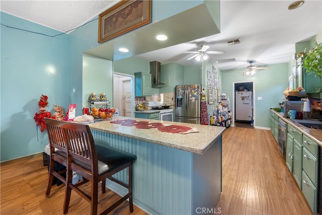 kitchen with wall chimney exhaust hood, stainless steel refrigerator with ice dispenser, white gas stove, light wood-type flooring, and ceiling fan