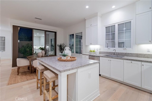 kitchen with white cabinetry, light wood-type flooring, light stone countertops, a kitchen island, and sink